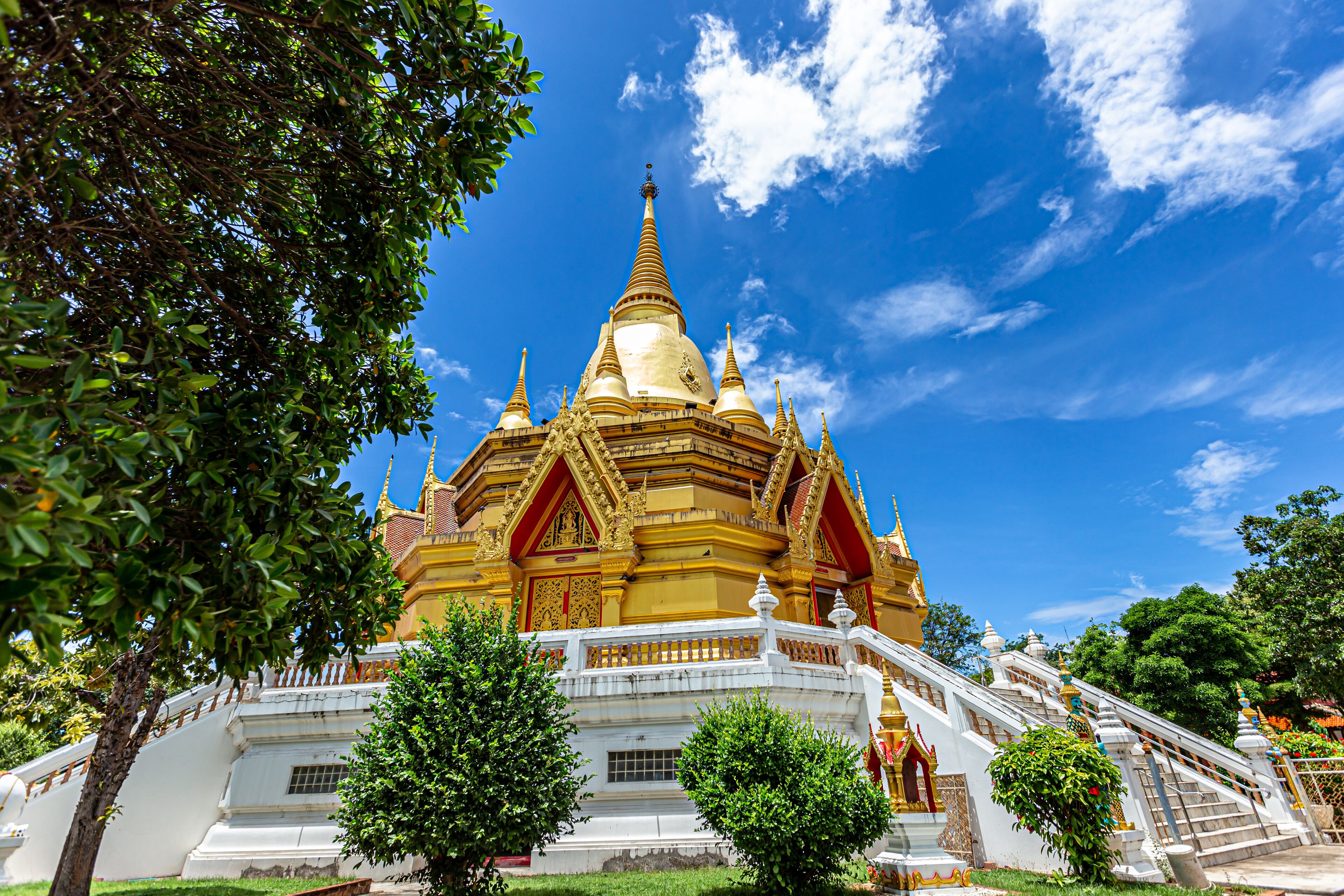 A golden temple with multiple spires, surrounded by trees and a clear blue sky.