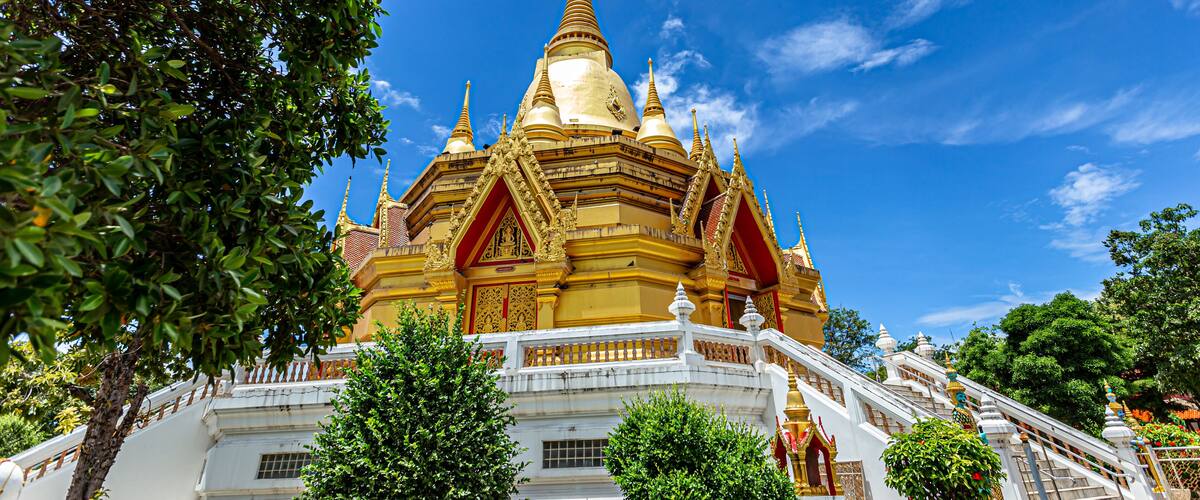 A golden temple with multiple spires, surrounded by trees and a clear blue sky.