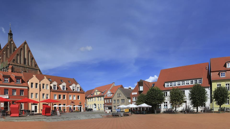 A historic town square with a prominent church, colorful buildings, and outdoor seating areas.