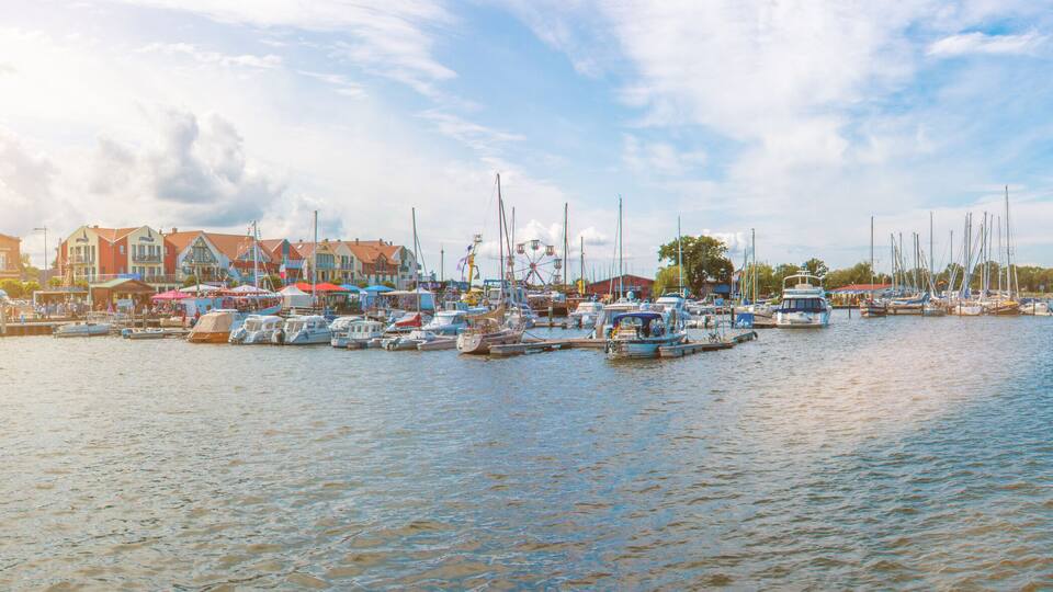 A marina with boats docked, a pier, and buildings in the background.