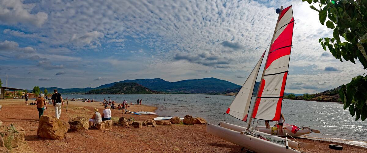 A sailboat on a sandy beach with people in the background and mountains in the distance.