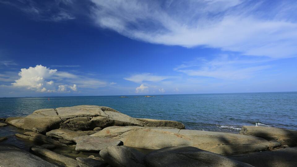 A rocky shoreline with large boulders and calm sea under a partly cloudy sky.