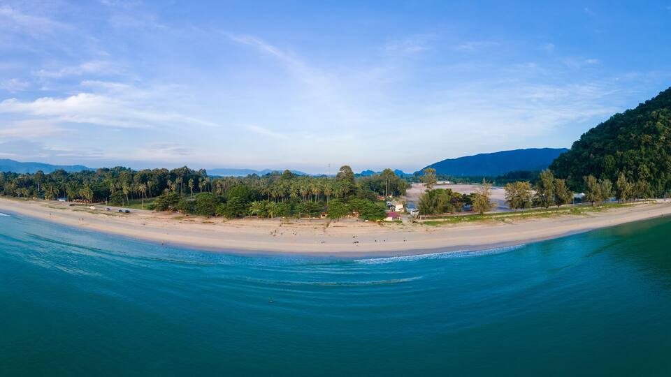 A coastal landscape with a beach, a forested hill, and a clear sky.