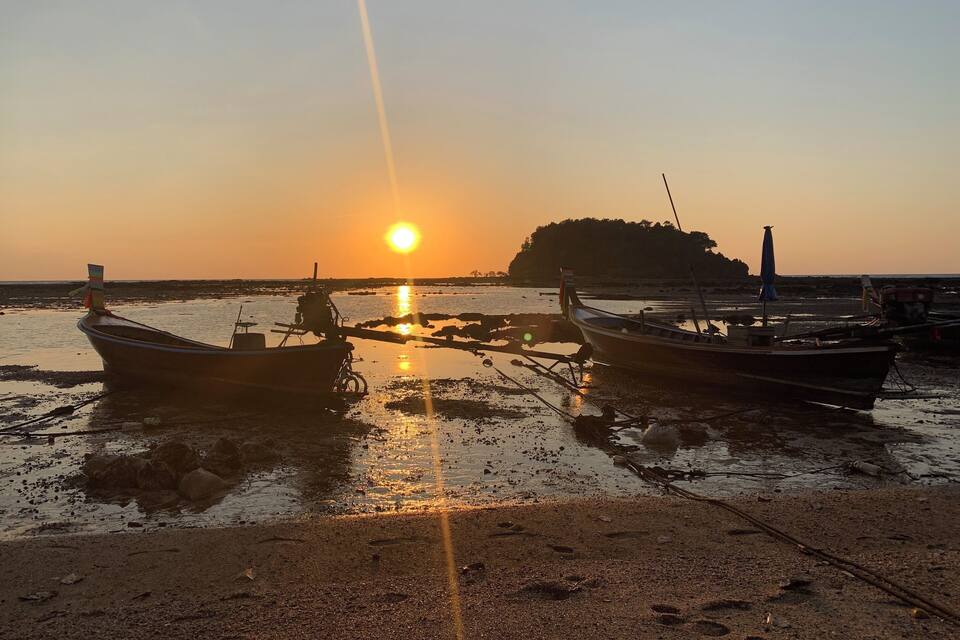 A sunset over a beach with boats and a small island in the background.