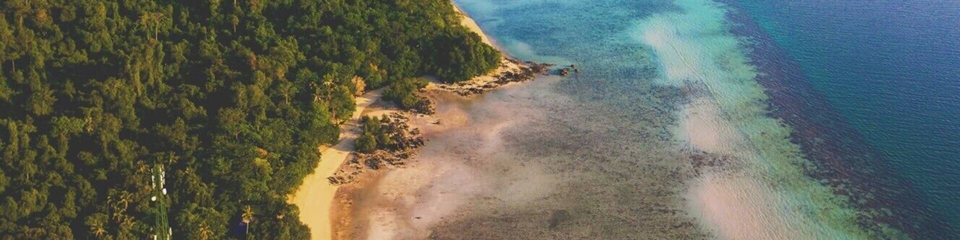 An aerial view of a coastal landscape with a forested island, a sandy beach, and a calm sea.