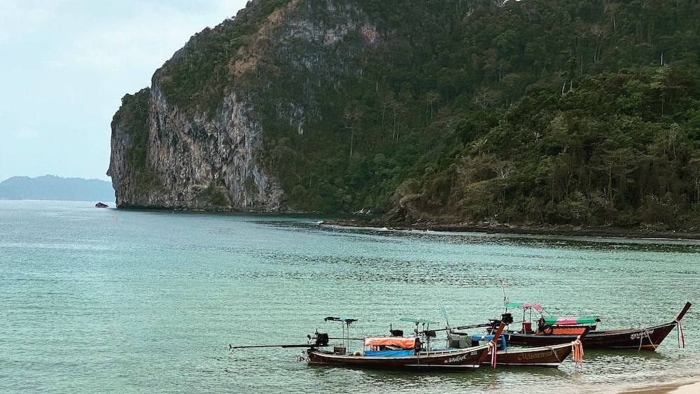 A beach with boats and a large cliff.