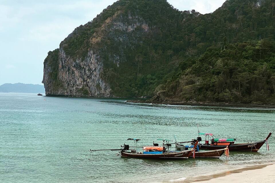 Una playa con barcos y un acantilado imponente.