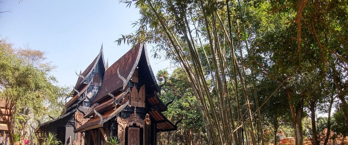 A traditional temple with intricate carvings and a multi-tiered roof, surrounded by bamboo trees and a dirt path.