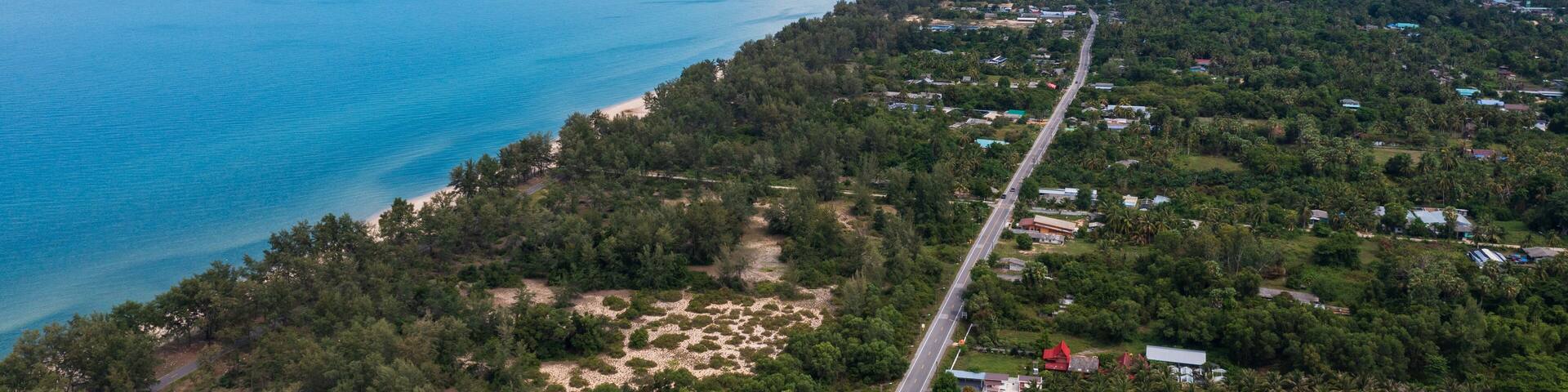 Aerial view of Sathing Phra coastline in Songkhla, Thailand. Long beach, turquoise sea, and lush green landscape meet a coastal road.