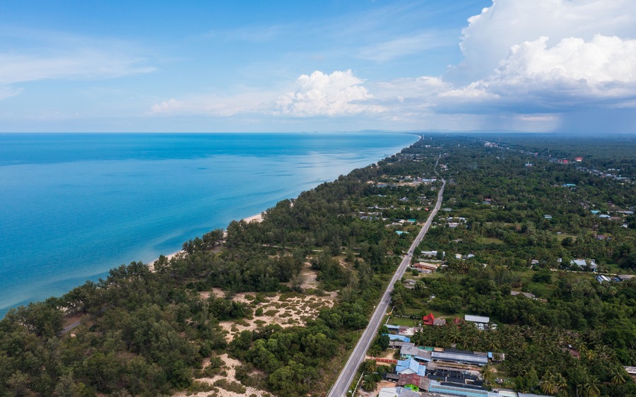 Aerial view of Sathing Phra coastline in Songkhla, Thailand. Long beach, turquoise sea, and lush green landscape meet a coastal road.