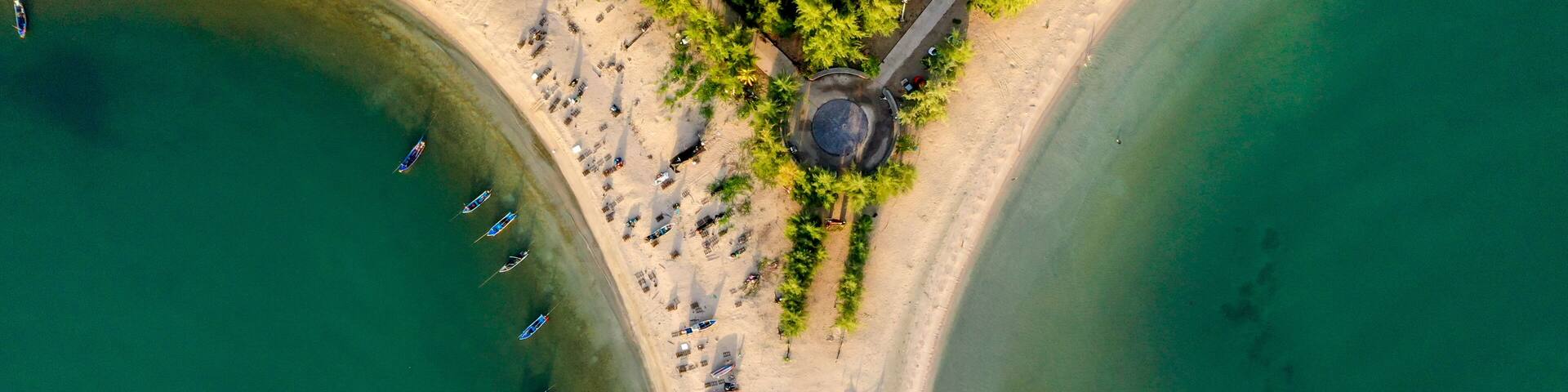An aerial view of a beach with boats, a circular structure, and a breakwater.
