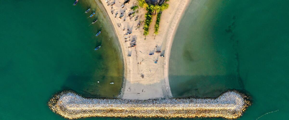 An aerial view of a beach with boats, a circular structure, and a breakwater.