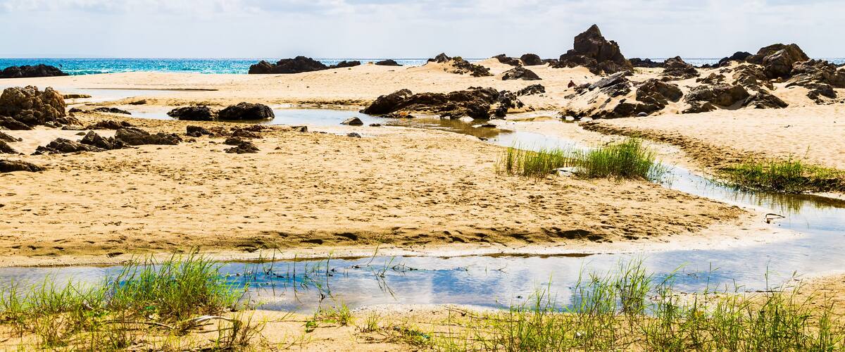 A beach with rocky outcrops, a small stream, and clear blue water.