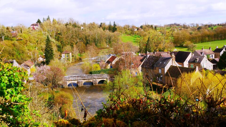 A village with a stone bridge over a river, surrounded by trees and houses.