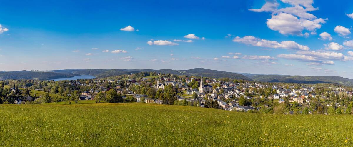 A town nestled in a valley with a lake and rolling hills in the background.