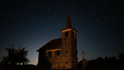 A church with a tall steeple under a starry night sky.