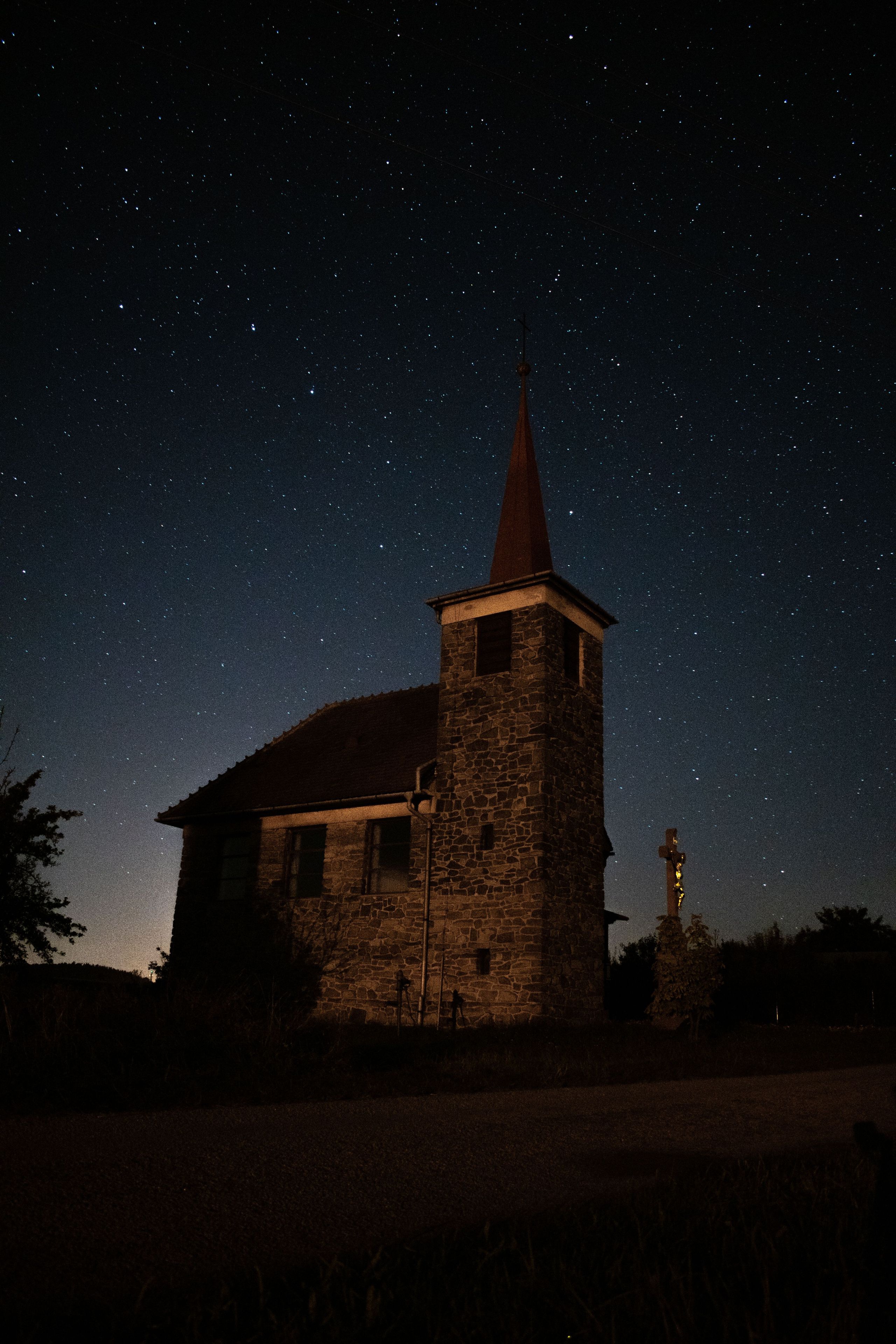 Una chiesa in pietra con un campanile a guglia sotto un cielo stellato.