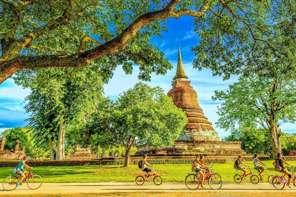 Een tempel omringd door bomen en mensen die op fietsen rijden.