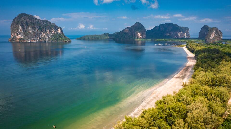 A coastal landscape with a sandy beach, clear turquoise waters, and several large limestone islands.
