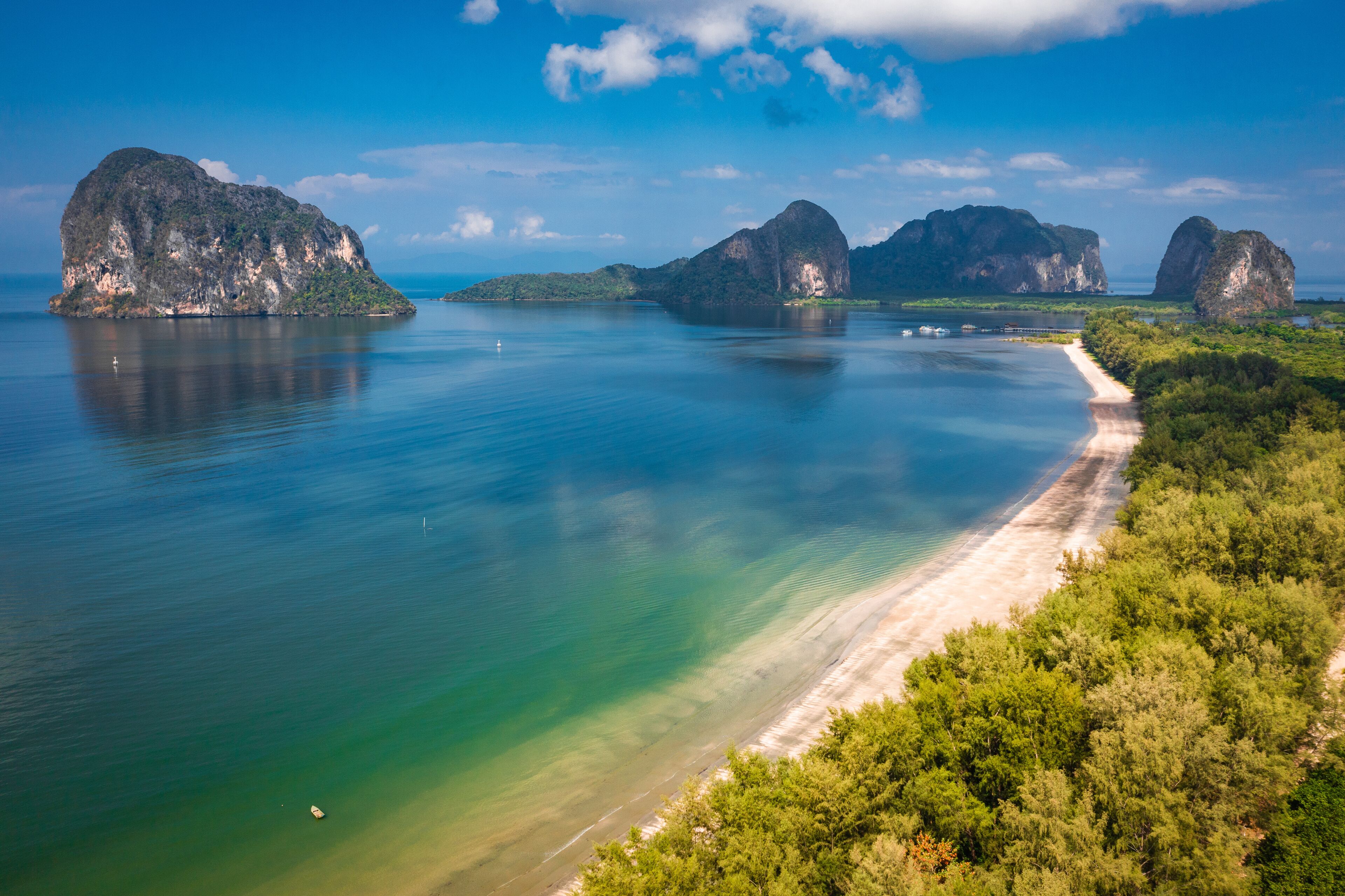 A coastal landscape with a sandy beach, clear turquoise waters, and several large limestone islands.