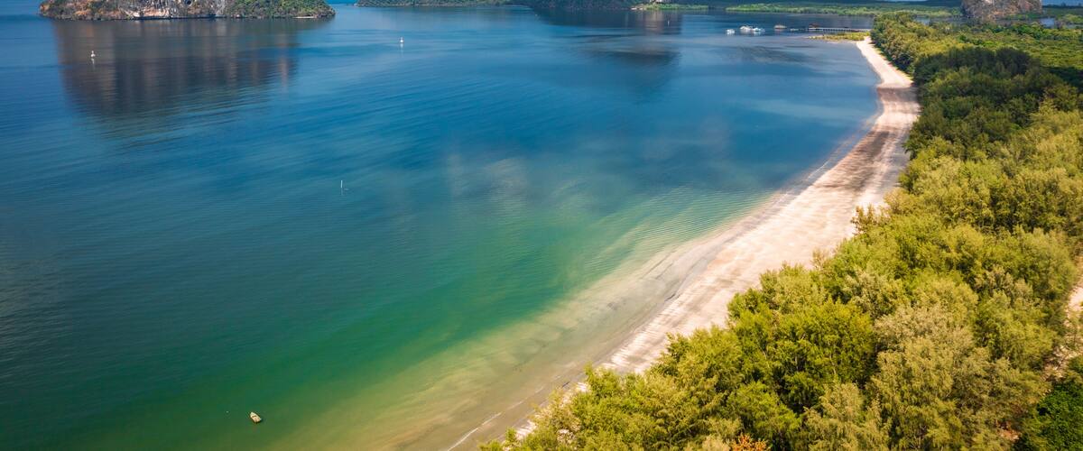 A coastal landscape with a sandy beach, clear turquoise waters, and several large limestone islands.
