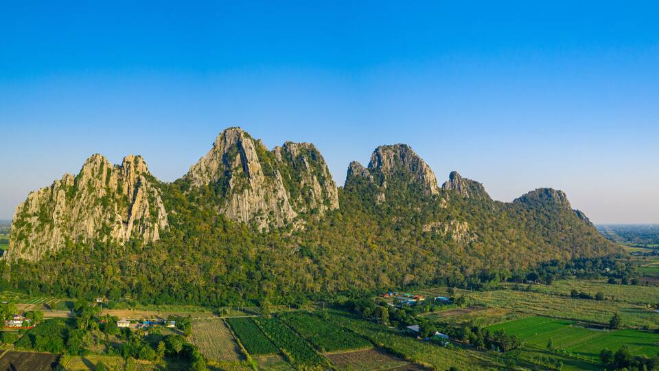 A mountainous landscape with rugged peaks and surrounding green fields.