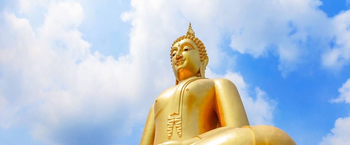 A large golden Buddha statue against a blue sky with clouds.