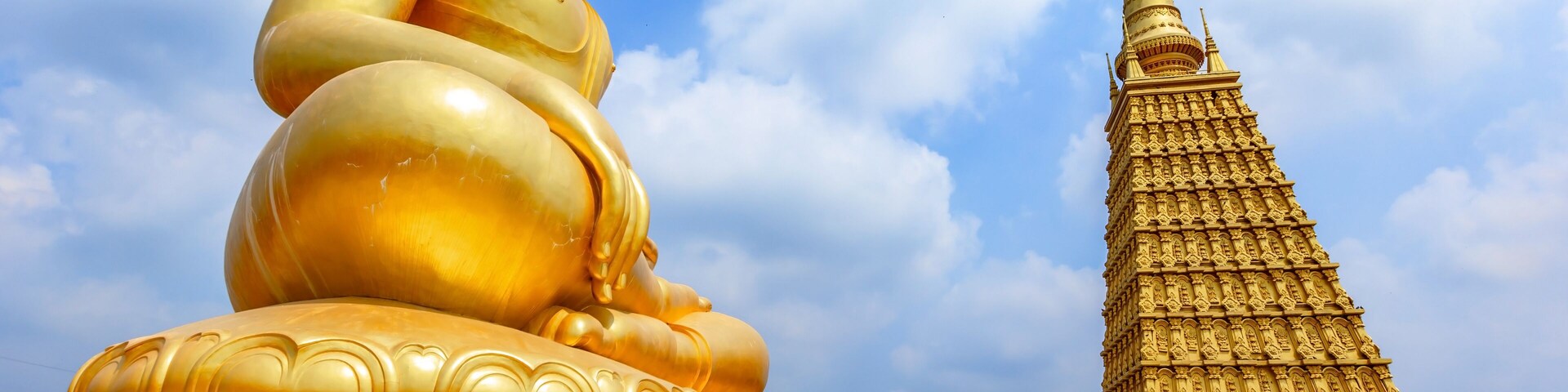 Una estatua dorada de Buda y una estupa dorada bajo un cielo azul.