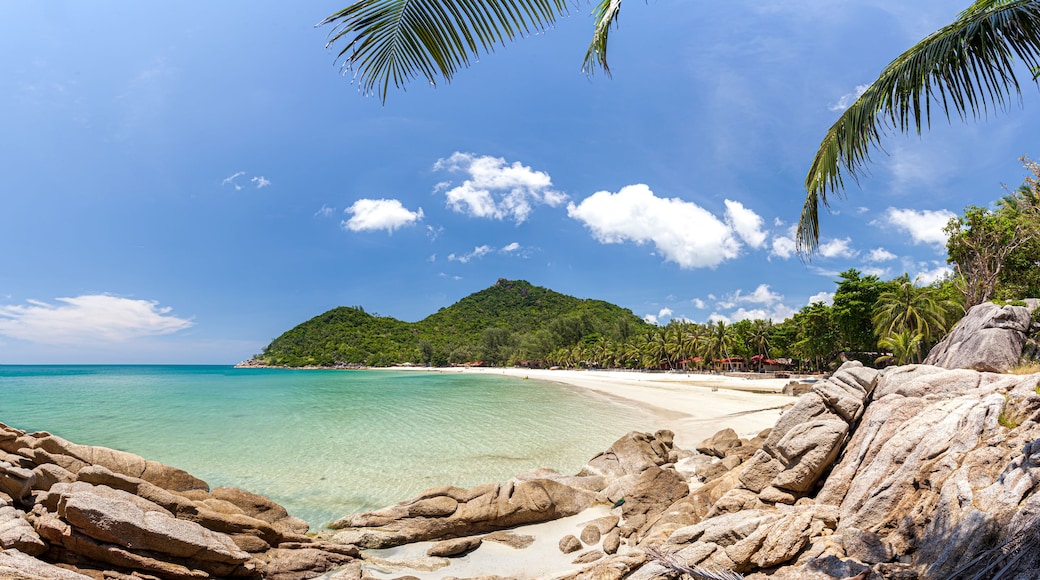 Una playa tropical con aguas turquesas cristalinas, costas rocosas y exuberante vegetación.