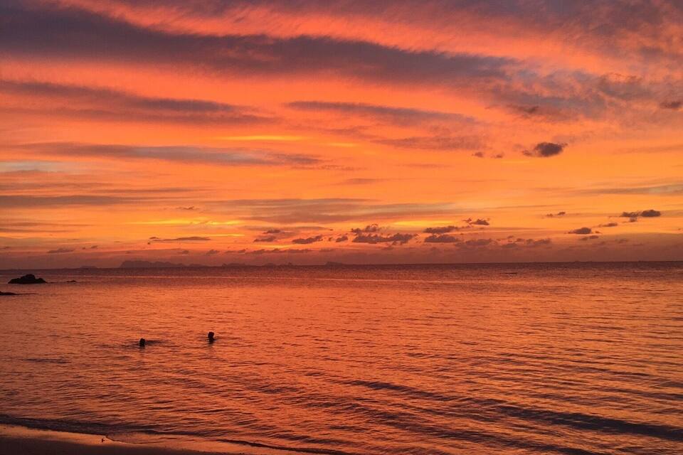 A sunset over a beach with calm waters and a clear sky.