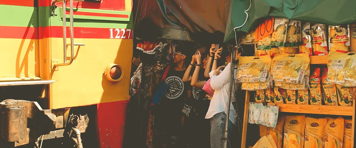 A train with a red and yellow exterior passing by a small roadside shop selling snacks.