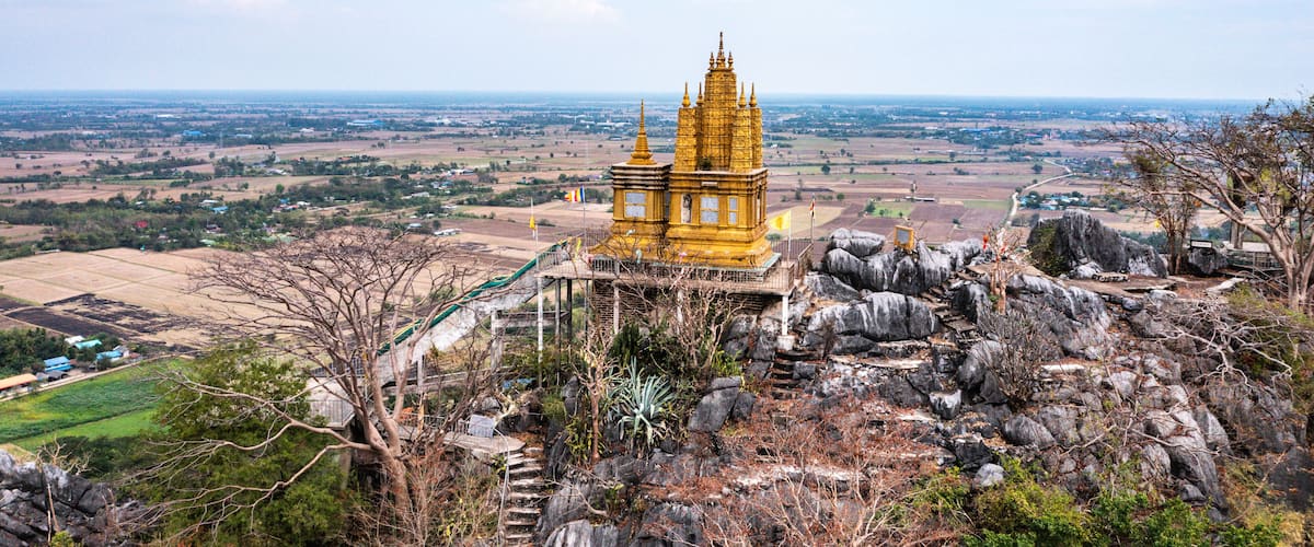 A golden temple on a rocky hill with a view of a rural landscape.