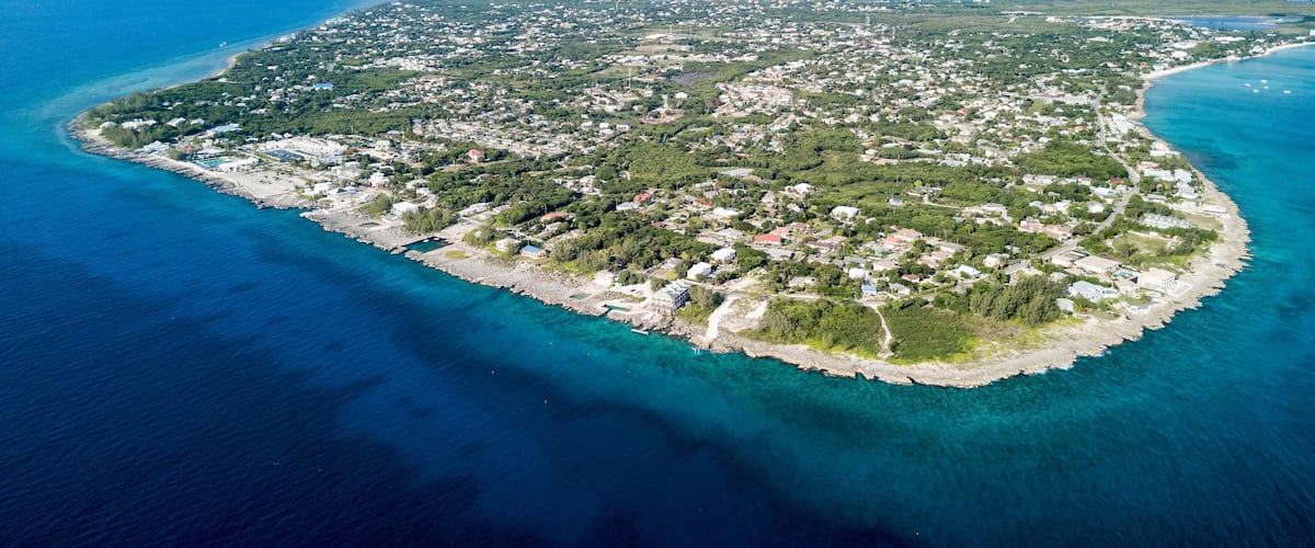 An aerial view of a coastal island with a dense settlement, clear blue waters, and a visible coastline.