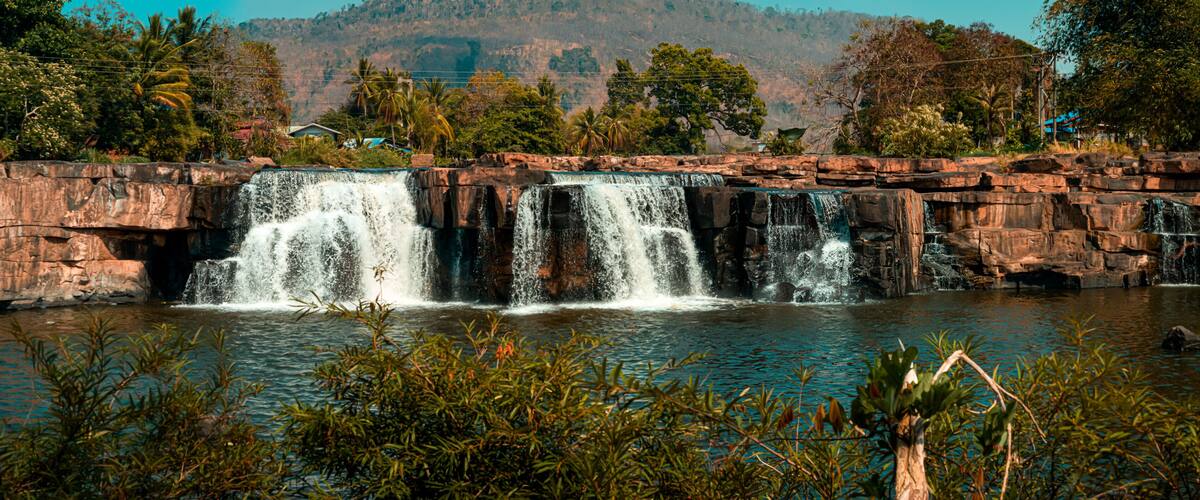 A waterfall cascading over rocky terrain with lush greenery and distant hills.