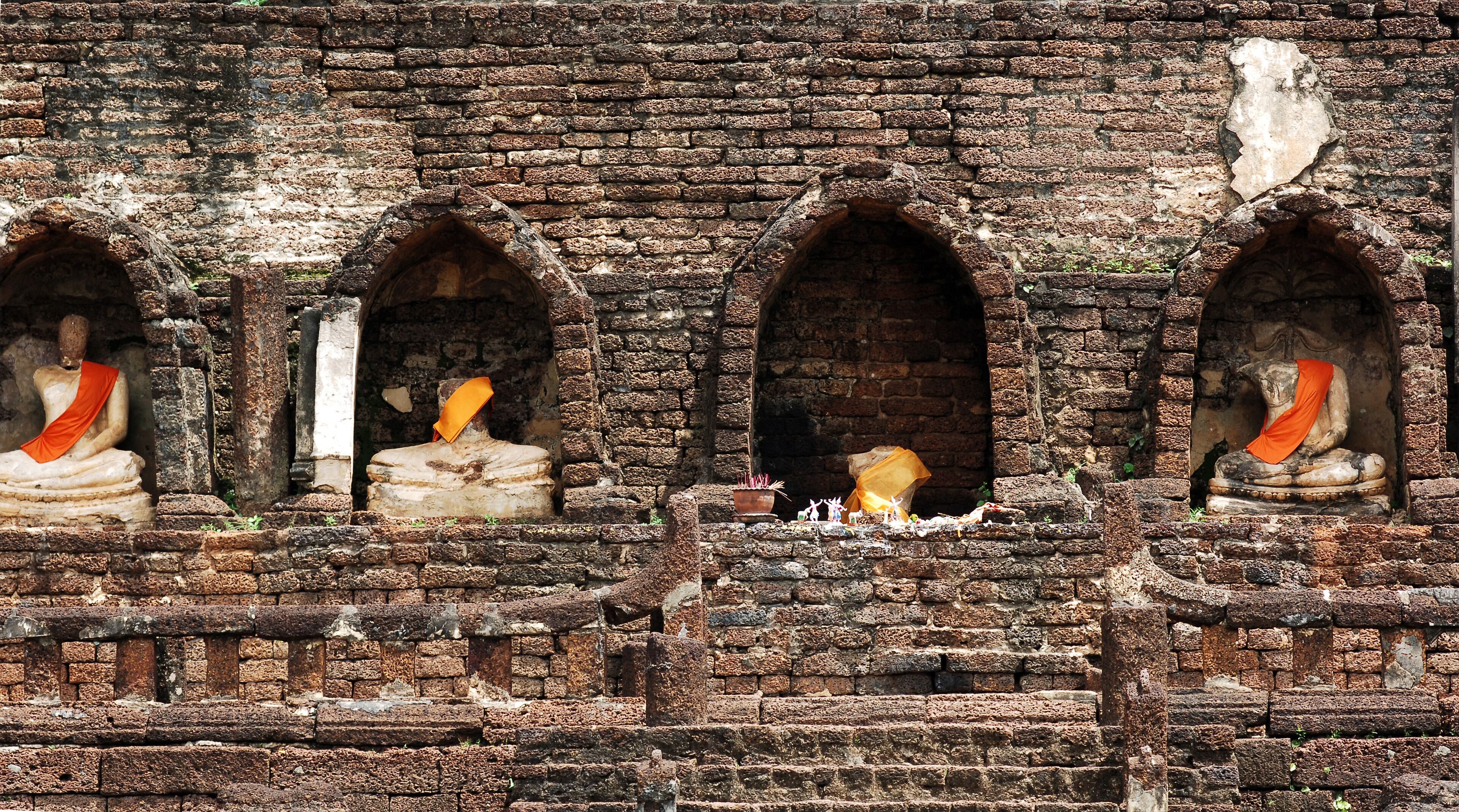 A temple with three Buddha statues in niches, each with a red cloth draped over them.