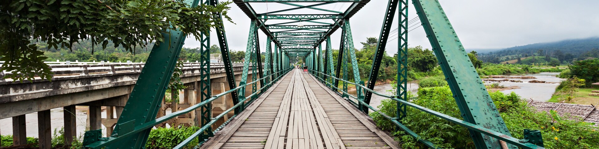 Un puente de metal verde con pasarela de madera que conduce a la orilla de un río.