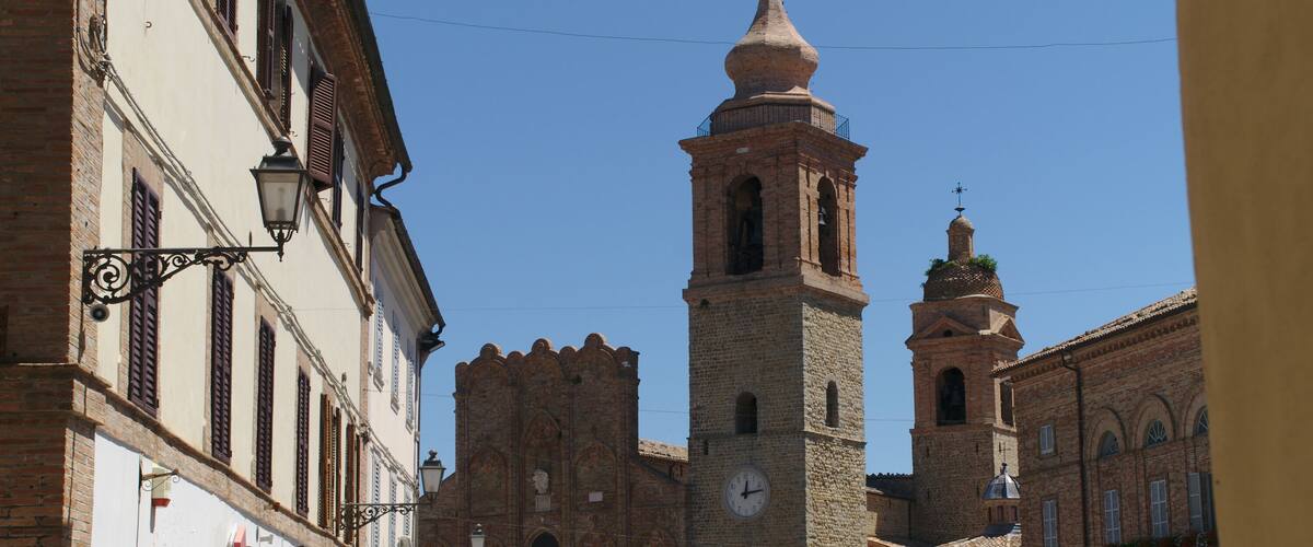 A historic square with a prominent clock tower, a statue, and traditional architecture.