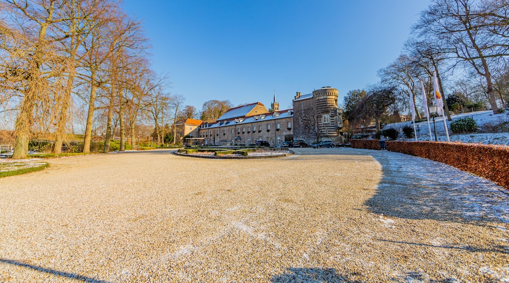 Esplanade of land surrounded by bare trees, shrubs with remnants of snow with Elsloo castle in the background, sunny winter day with a blue sky in Elsloo, South Limburg, Netherlands