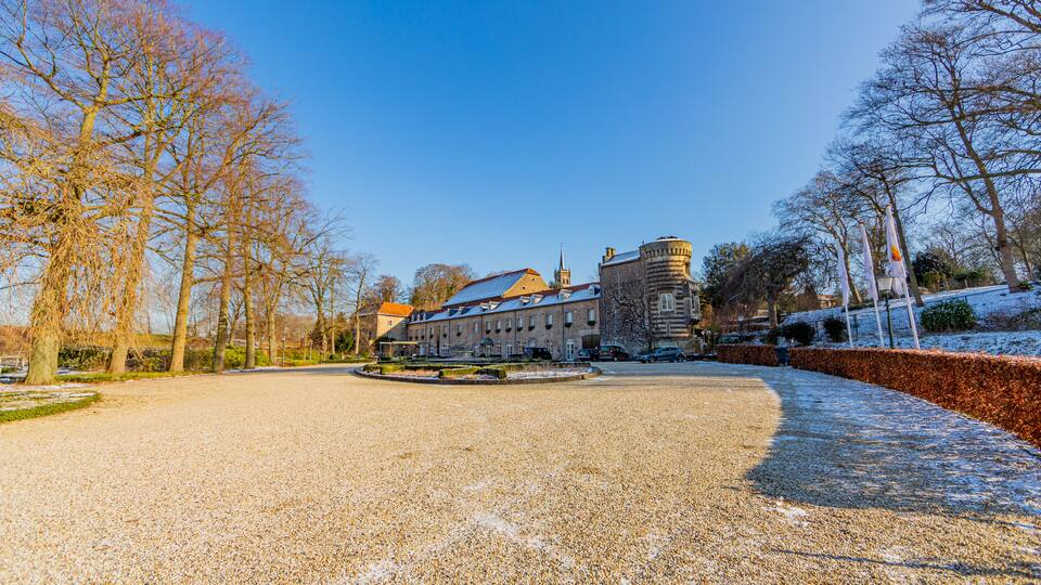 A gravel path leading to a historic building with a tower, surrounded by leafless trees and a clear blue sky.