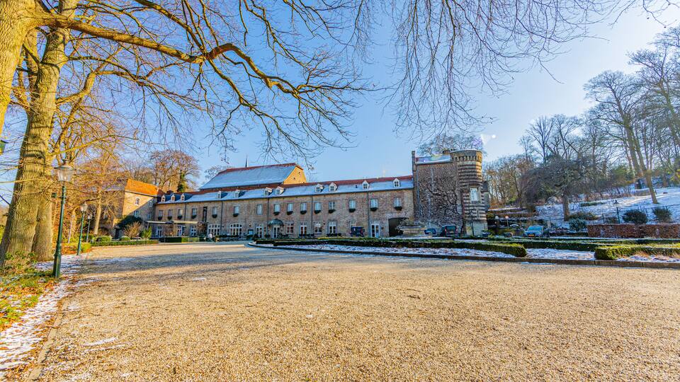 A large building with a tower, surrounded by trees and a gravel path.