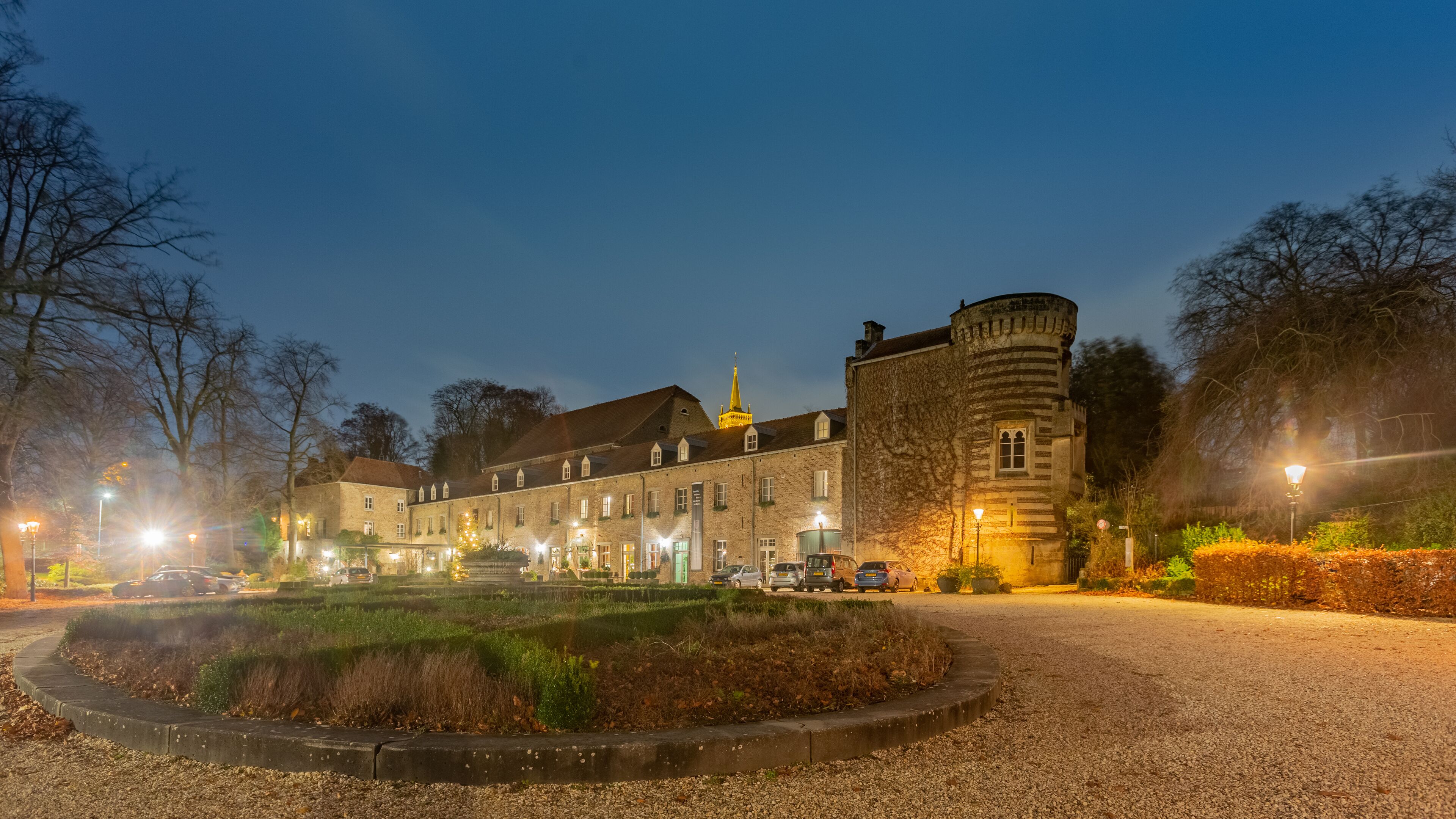 A historic building with a tower, surrounded by a well-maintained garden and a gravel path.