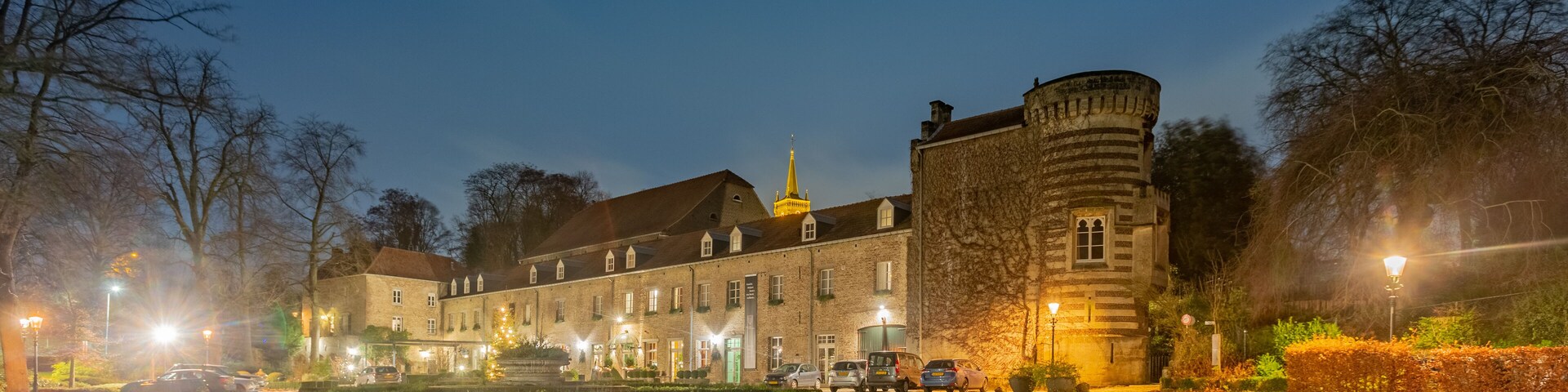 A historic building with a tower, surrounded by a well-maintained garden and a gravel path.