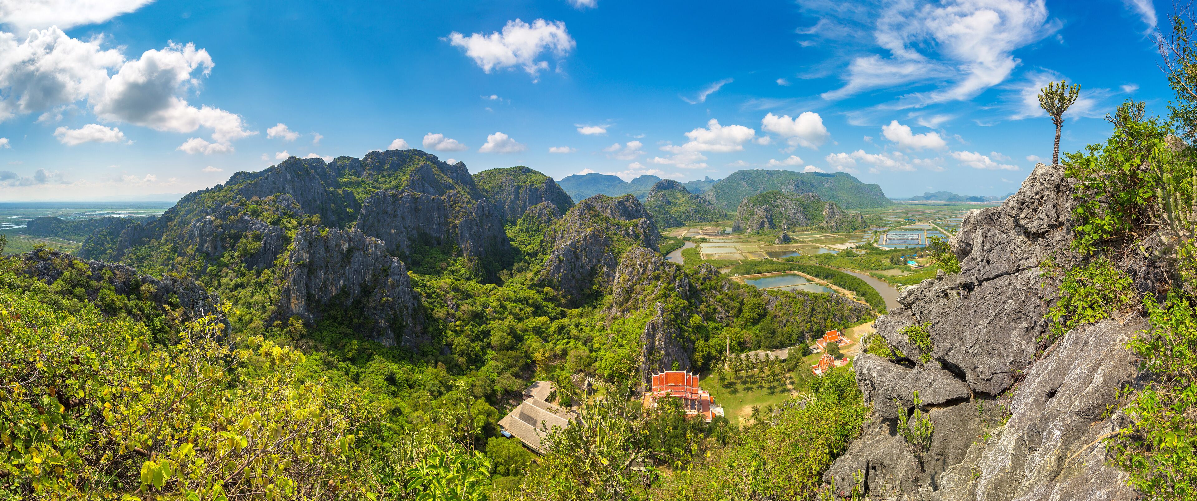 A mountainous landscape with lush greenery, rocky cliffs, and a temple with a red roof.