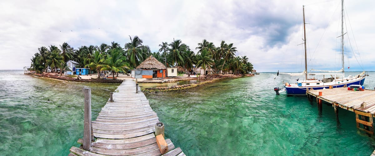 A wooden pier leading to a small island with thatched-roof huts and palm trees.
