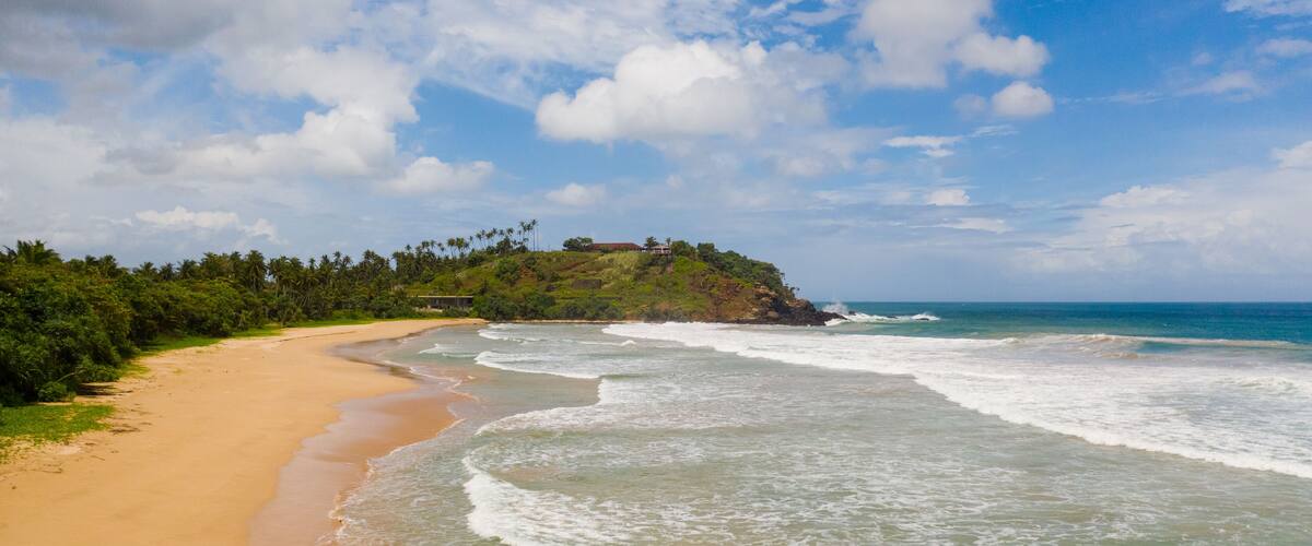 A beach with a sandy shore, gentle waves, and a hill with vegetation.