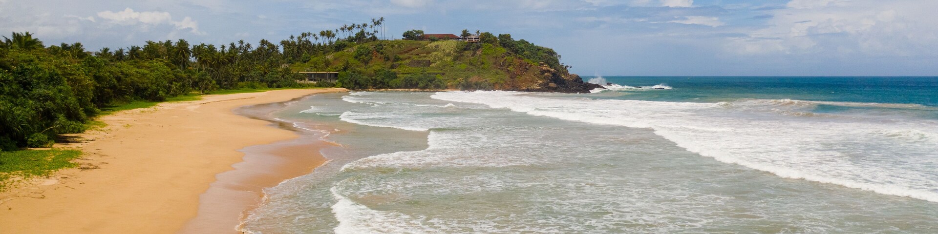 A beach with a sandy shore, gentle waves, and a hill with vegetation.