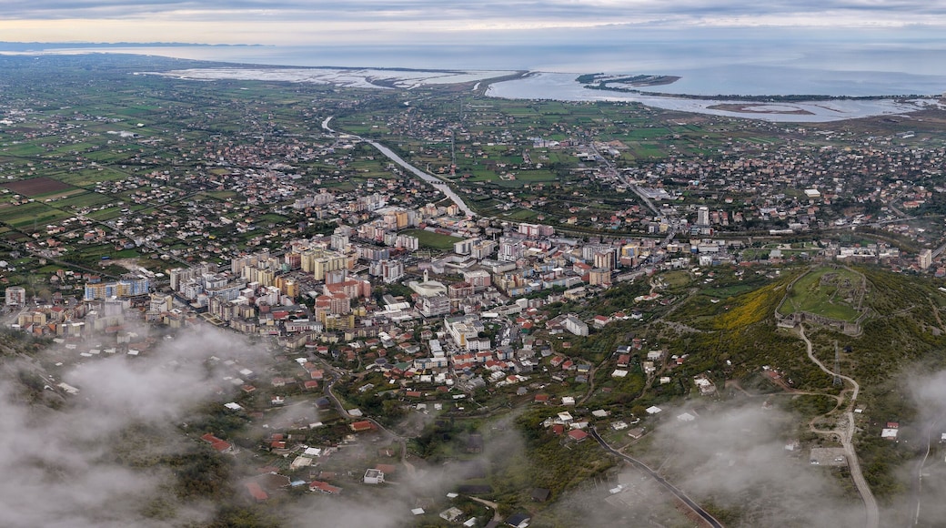 Wide aerial panorama showing Lezhë, Lezhë Castle, the Drin River, and Shëngjin stretching to the Adriatic Sea under cloudy skies.