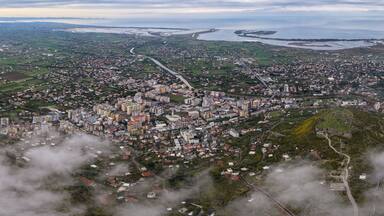 Wide aerial panorama showing Lezhë, Lezhë Castle, the Drin River, and Shëngjin stretching to the Adriatic Sea under cloudy skies.