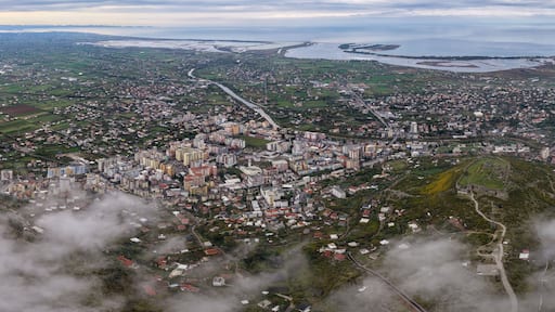 Wide aerial panorama showing Lezhë, Lezhë Castle, the Drin River, and Shëngjin stretching to the Adriatic Sea under cloudy skies.