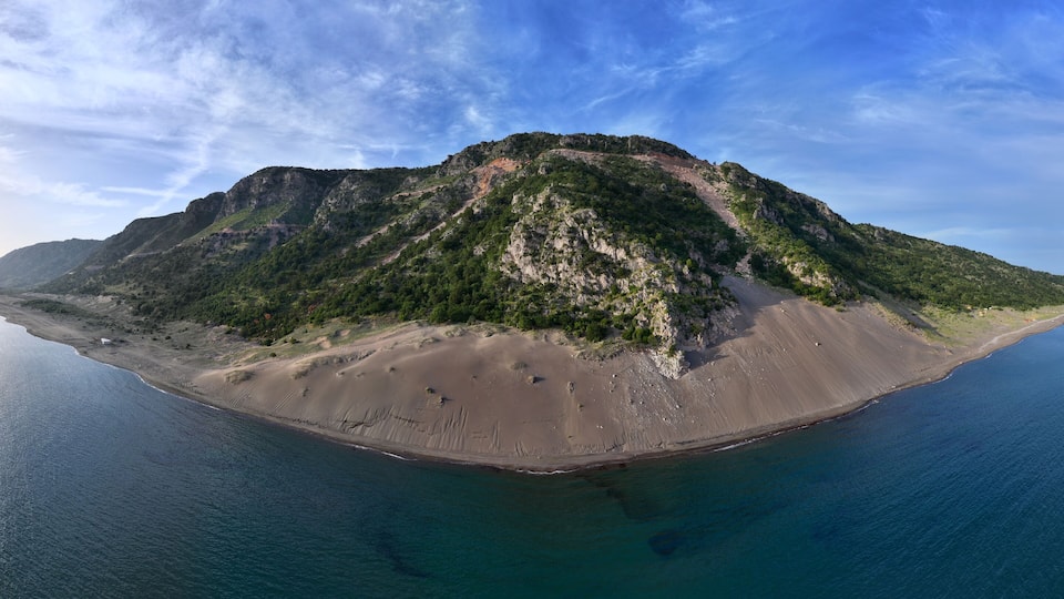 An aerial view of a large island with a prominent mountain, a sandy beach, and a calm sea.